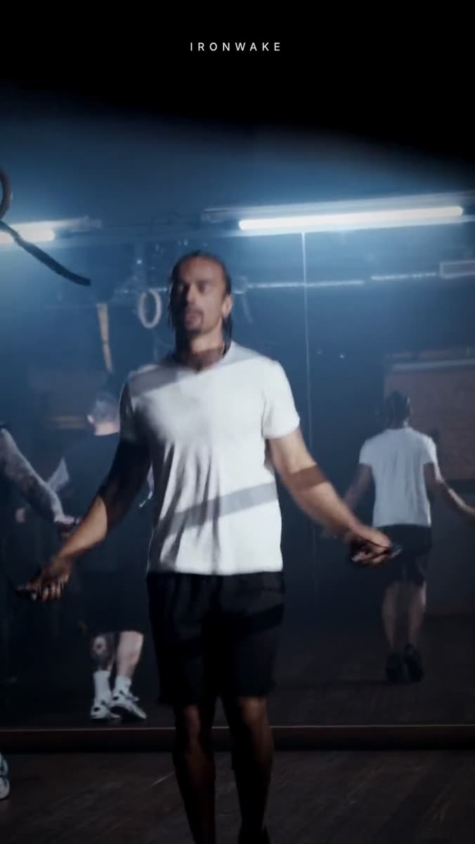 A dark gym in backlit haze, a man mid-skip with a jump rope, other people skipping behind him, and a small letterspaced wordmark set across the top of the frame